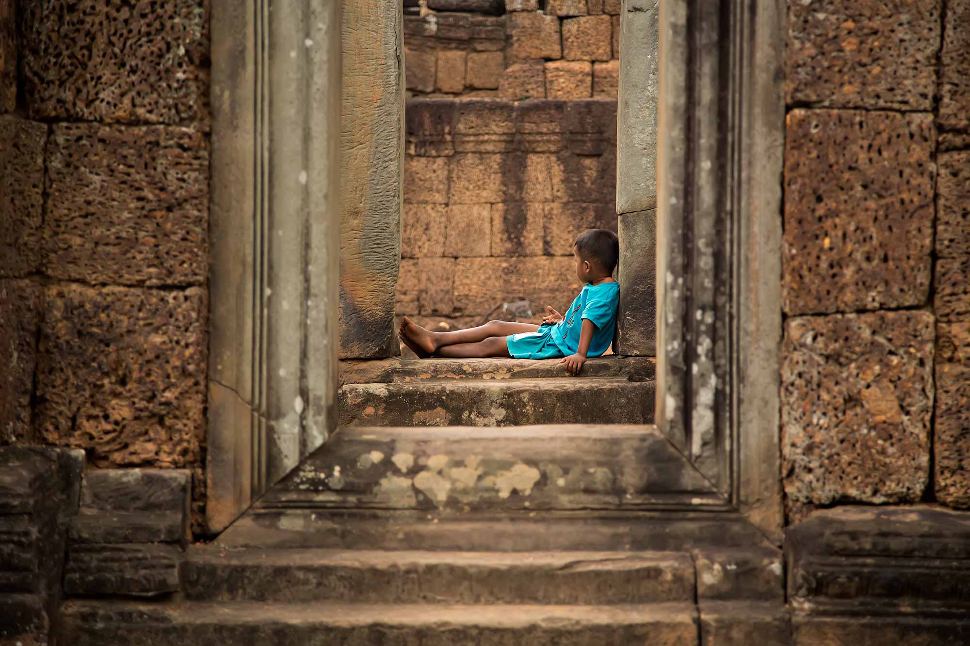 A boy sitting inside East Mebon temple in Angkor Wat, Cambodia. © Ulli Maier & Nisa Maier